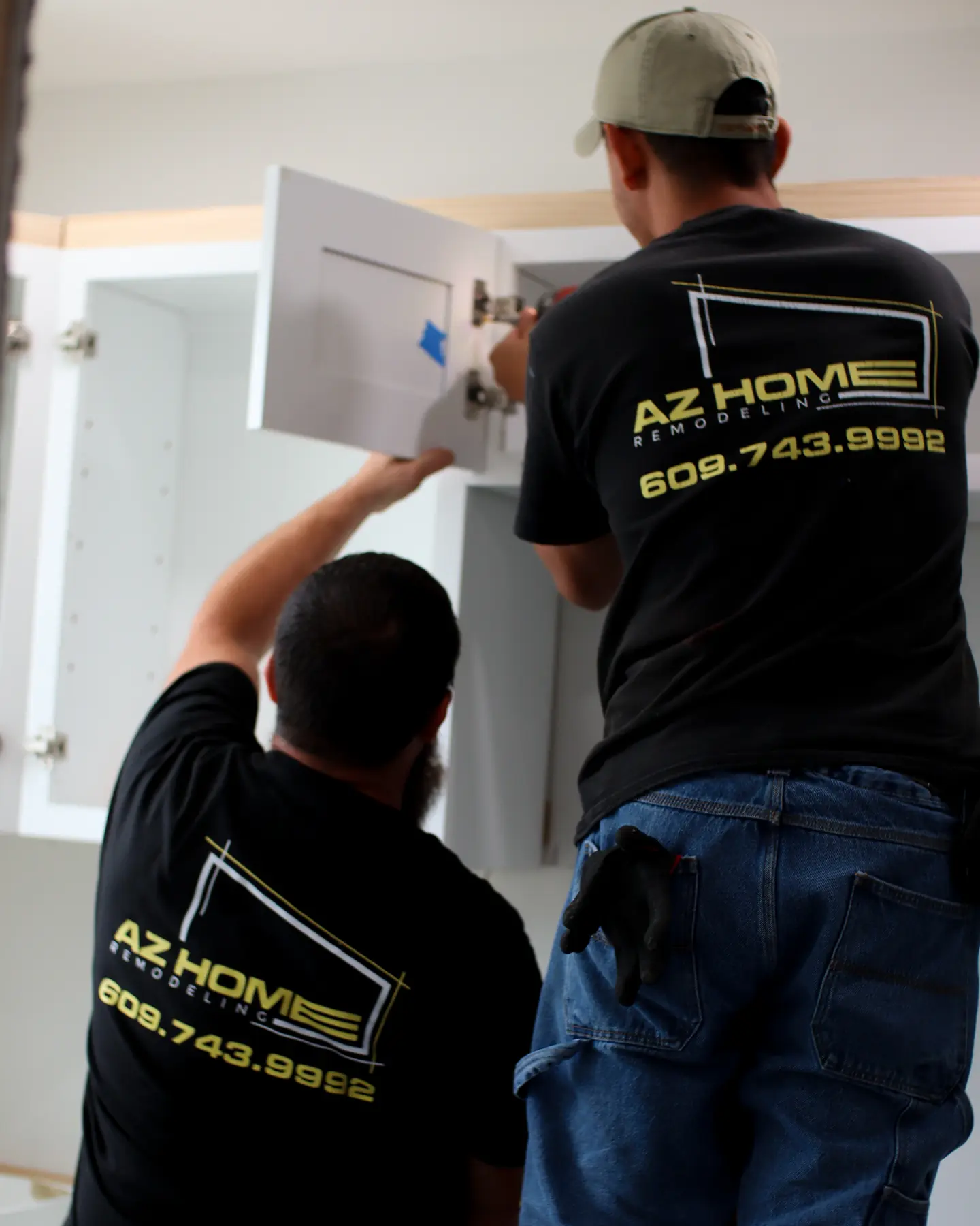 Two AZ Home Remodeling installers in branded shirts fitting a cabinet door during a kitchen remodel
