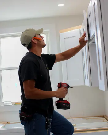AZ Home Remodeling installer in a cap mounting a kitchen wall cabinet with a drill