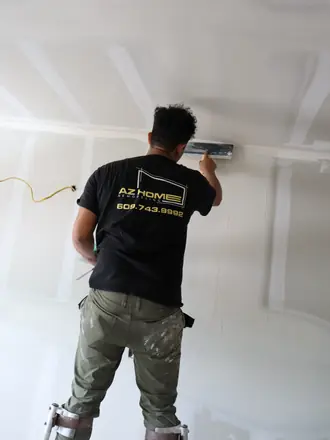 AZ Home Remodeling installer on a step ladder fitting a ceiling vent in a freshly drywalled room