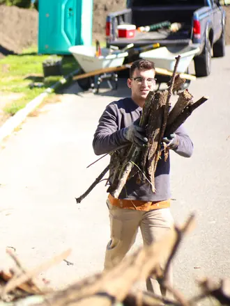 Lawns By Rainey crew member carrying an armload of branches off a job site