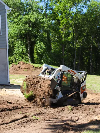 Lawns By Rainey skid steer pushing a pile of dirt while grading a new-build lot