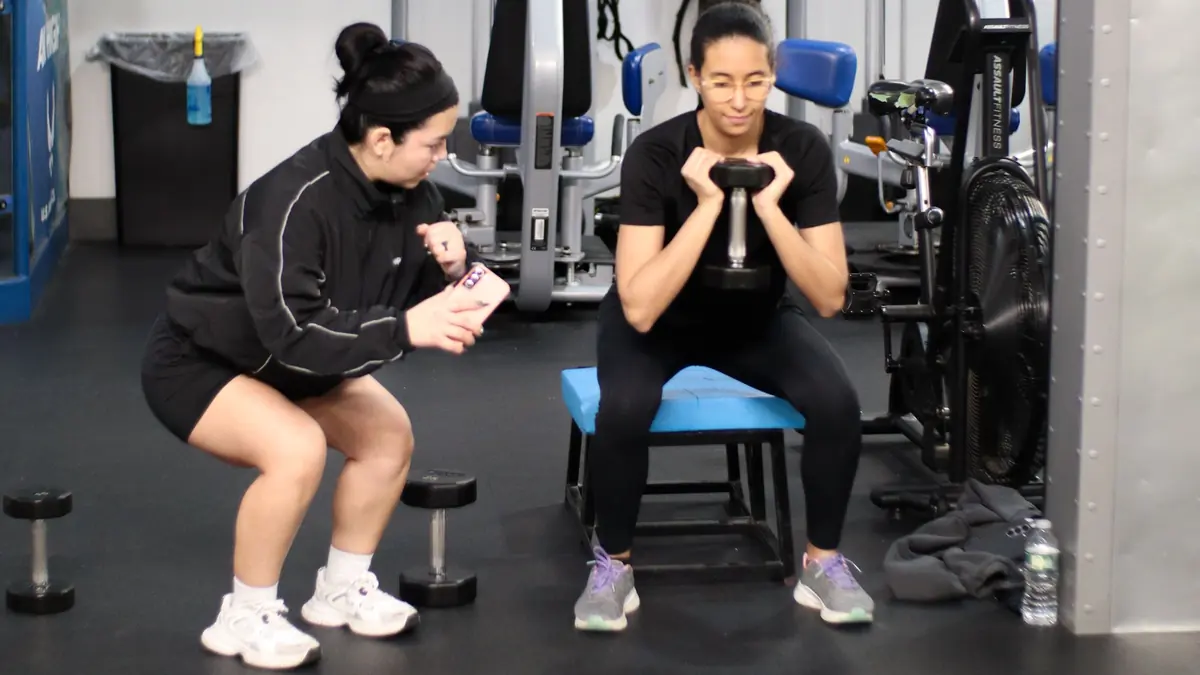 PowerHaus Fitness coach Andrea checking her notes while a client holds a kettlebell squat