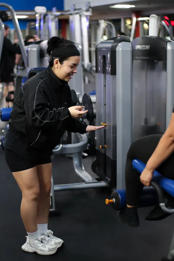 PowerHaus Fitness coach Andrea laughing while guiding a client on a weight machine